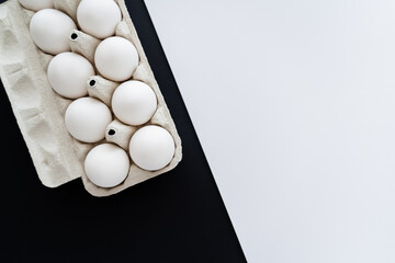 Poster - Top view of natural chicken eggs in carton tray on white and black background with copy space.