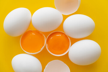 Poster - Top view of organic yolks in shells and white eggs on yellow background.