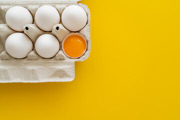 Poster - Top view of yolk in shell near eggs in cardboard box on yellow background.