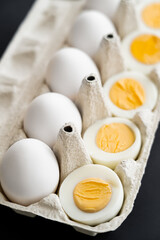 Poster - Close up view of cut boiled and raw eggs in blurred carton tray isolated on black.