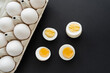 Top view of boiled and raw eggs in cardboard container on black surface.