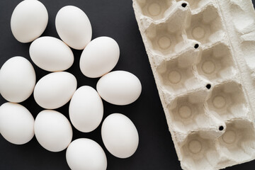 Poster - Top view of carton tray and white eggs on black background.