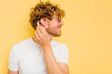 Wall Mural - Young caucasian man wearing hearing aid isolated on yellow background