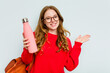 © Asier - Young student woman holding a canteen isolated on blue background showing a copy space on a palm and holding another hand on waist.