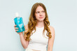 © Asier - Young caucasian woman holding a mouthwash isolated on blue background confused, feels doubtful and unsure.