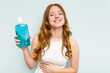 © Asier - Young caucasian woman holding a mouthwash isolated on blue background laughing and having fun.