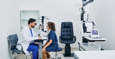 Wall Mural - Pediatric ophthalmology. Optometrist checking eyesight of boy patient at modern eye clinic