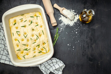 Wall Mural - Raw focaccia dough in a baking dish. Traditional Italian Focaccia with rosemary on a dark background. banner, menu, recipe place for text, top view