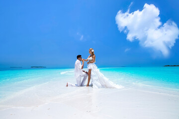 Summer love. Beautiful happy young couple in wedding clothes is standing on a beach in the Maldives. Engagements and wedding on the beach on the paradise island of Maldives. Luxury travel.