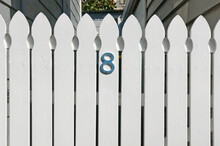 Closeup Of A White Picket Fence With House Address Number Eight In Blue Wood