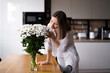 © arthurhidden - Happy and joyful young woman in white arranging white flowers at home in the kitchen