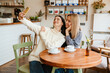 Leinwandbild Motiv White women smiling and taking selfie on cellphone in cafe