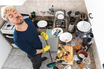 Man sweeping with broom complaining about cleaning messy kitchen