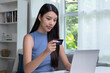 © amenic181 - Young Asian woman holding credit card and using laptop computer. Businesswoman working at home. Online shopping, e-commerce, internet banking, spending money, working from home concept