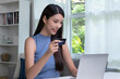 © amenic181 - Young Asian woman holding credit card and using laptop computer. Businesswoman working at home. Online shopping, e-commerce, internet banking, spending money, working from home concept