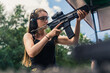 © PoppyPix - young woman practicing shooting on target and holding a black rifle, medium shot. High quality photo