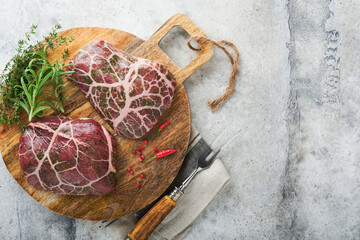 Steaks Raw. Raw cowboy steak, marbled beef meat with spices rosemary and pepper on old wooden board on old grey slate table background. Top view. Mock up.