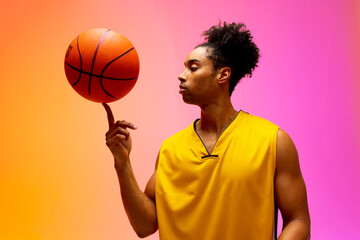 Image of biracial basketball player spinning basketball on pink to orange background