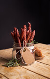 Fototapeta Tulipany - Polish kabanosy sausages in a jar. Thin dry sausages with blank label in a rural, eco composition, on black background.