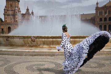 Canvas Print - Young teenage woman in white suit with black polka dots, dancing flamenco in front of water fountain and surrounded by soap bubbles. Flamenco concept, dance, art, typical Spanish dance, bubbles.