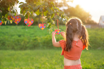 A girl standing with her back decorates a tree with heart-shaped postcards with colorful puzzles inside as a sign of support for children suffering from autism syndrome