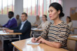 © JackF - Portrait of focused young adult female sitting at desk studying in classroom with colleagues