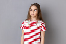 Portrait Of Funny Silly Little Girl Wearing Striped T-shirt Looking Up Cross Eyed With Stupid Dumb Face, Girl Has Awkward Confused Comical Expression. Indoor Studio Shot Isolated On Gray Background.