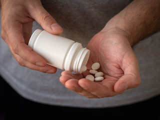 The man pours large white pills into the palm of his hand from a white plastic jar. Treatment and prevention of diseases