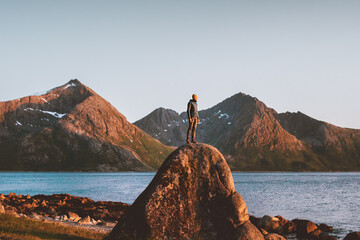 Wall Mural - Man traveling in Norway outdoor adventure lifestyle sunset mountains landscape tourist standing alone on rock freedom concept