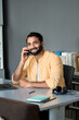 © insta_photos - Happy smiling ethnic indian professional business man sitting at work desk talking on cell phone, eastern businessman making mobile phone call by cellphone working at home or in office. Vertical