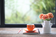 Orange Roses And Small Coffee Cup And Notebook Pencil On Wooden In Front Of Windows