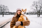 Fototapeta Miasto - Cute young girl is having fun in winter park with her dog on bright day. Woman relaxing outdoors