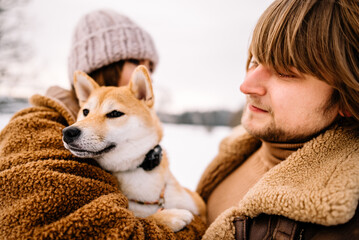 Cute young couple having fun in the winter park with their dog on bright day.Man and woman are relaxing