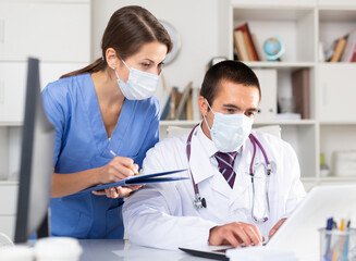 Wall Mural - Doctor and nurse in protective medical mask check patient data in hospital computer database