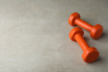 Orange vinyl dumbbells on light grey table. Space for text