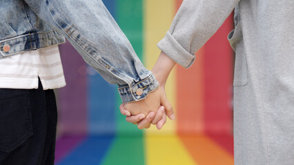 Closeup young adult queer transgender lover asia two people hold hand with colorful stripes flag. Proud of LGBT or LGBTQIA partner culture hug love sign in bisexual festival march day at city street.