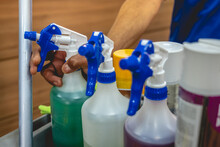 Hand Of Young Janitorial Worker Holding A Sprayer With Cleaner In Trolley Of Cleaning Supplies