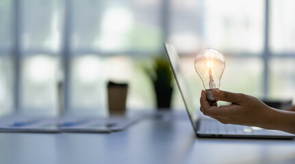 Close-up of a man holding a glowing light bulb with icons of ideas, innovation and business inspiration. Cyber ​​digital data saves energy