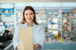 © 2B - A young pharmacist presents a paper bag containing medicines to sell in a general pharmacy.