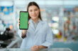 © 2B - Young pharmacist standing smiling looking at the camera holding a phone in front of a green screen