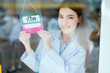 © 2B - Pharmacist in front of a shop with an 'open' sign in Thailand. looking out the glass window