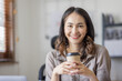 © David - Happy indian girl asian woman drinking hot coffee in workplace an home office.