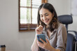 © David - Photo of a joyful nice Asian indian woman using a smartphone with a laptop and smiling while sitting in workplace an home office.