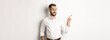© Mix and Match Studio - Young bearded guy seeing something disturbing, cringe while pointing finger left at promo offer, standing awkward against white background