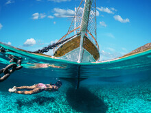 Girl Diver Is Snorkeling On A Beautiful Sea Beach. The Bottom Half Of The Picture Is Occupied By The Seabed, On The Top - The Coast With A Yacht And A Beautiful Sky.