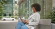 © South House Studio - African American business woman with curly hair and glasses sitting outside with laptop and chatting, enjoying her time