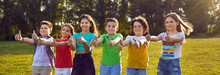 Group Portrait Of Happy Cheerful Children Enjoying Cool Summertime Trip To Countryside, Having Great Leisure Time, Standing In Line On Green Meadow Or Field Grass, Doing Thumbs Up Gesture And Smiling