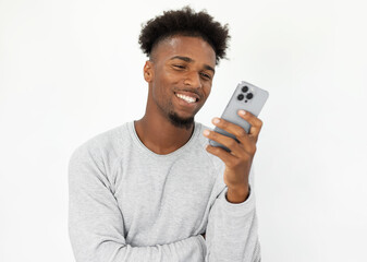 Portrait of happy African American man using social network on mobile phone. Young bearded guy wearing white sweater reading message on smartphone and smiling. Mobile technology concept