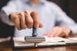 © chokniti - Close-up of a person's hand stamping with approved stamp on certificate document public paper at desk, notary or business people work from home, isolated for coronavirus COVID-19 protection