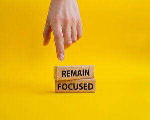 Remain focused symbol. Concept words Remain focused on wooden blocks. Beautiful yellow background. Businessman hand. Business and Remain focused concept. Copy space.